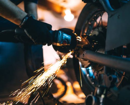 Motorcycle repair after welding with spark. Young man repairing motorbike in garage.
