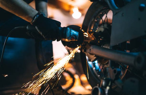 Motorcycle repair after welding with spark. Young man repairing motorbike in garage.